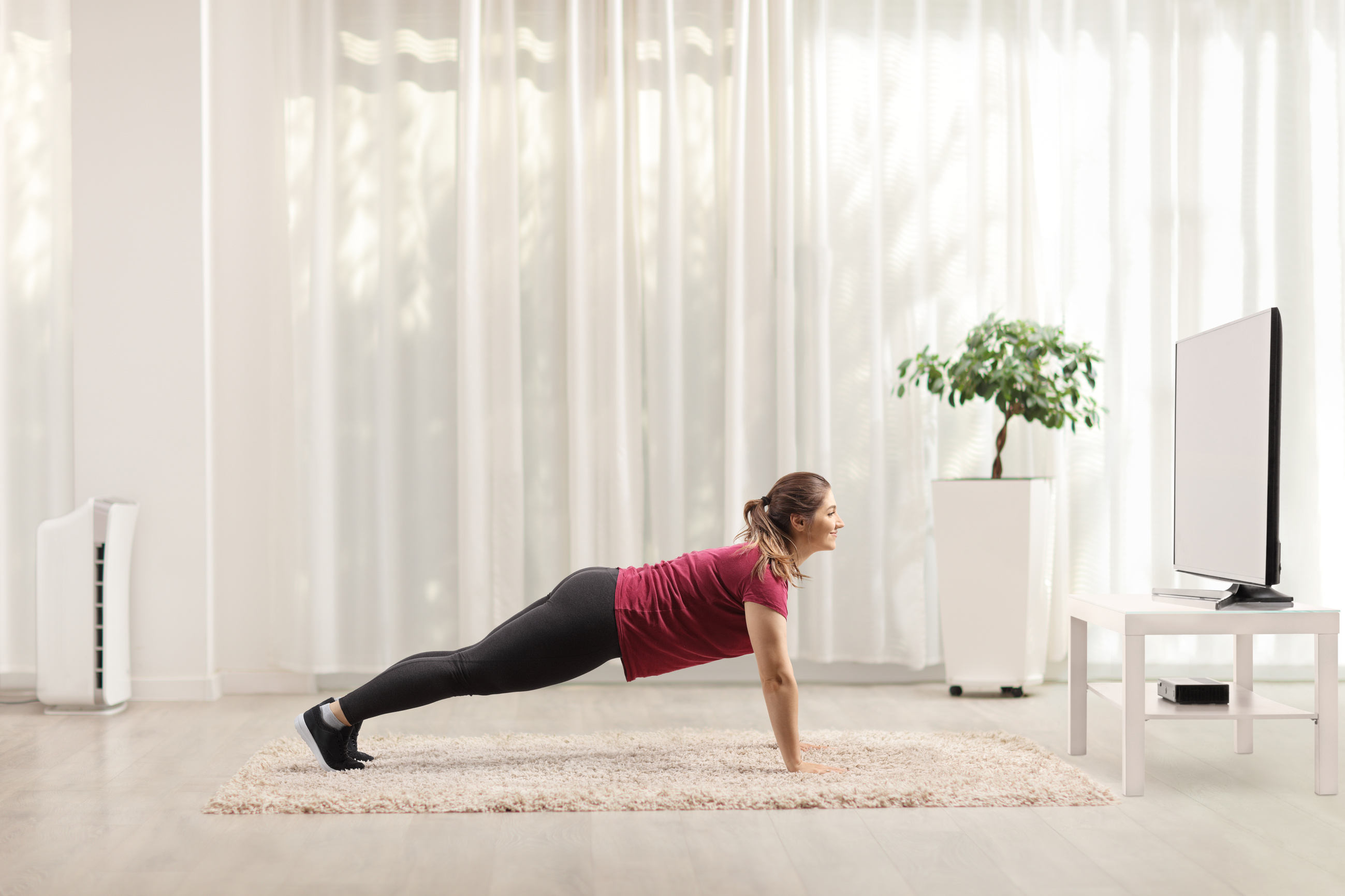 Young woman doing plank exercises in front of a tv